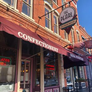 Street view of The Pearl Ice Cream Parlor. A sign outlined in an ice cream cone hangs from the building. 