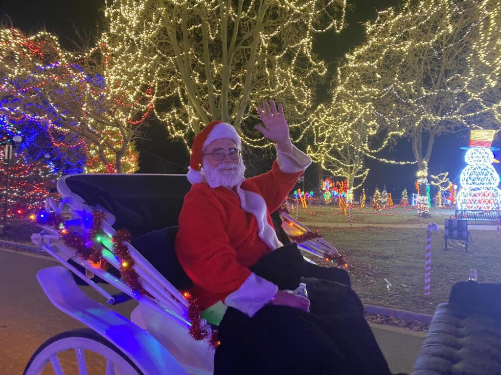 Santa waves as he rides in a carriage at Rotary Lights, La Crosse holiday light display.