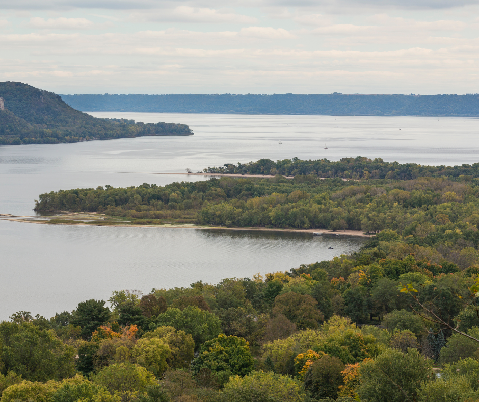 a bluff off in the distance with tree-covered land in the forefront with a winding Mississippi River through the center and a cloud-filled sky