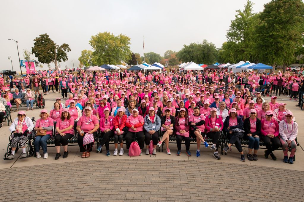 A large crowd of participants dressed in pink gathers at Riverside Park in La Crosse, Wisconsin, for the Steppin’ Out in Pink breast cancer awareness walk.